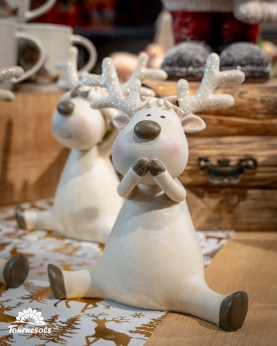 Deux figurines de rennes blancs aux bois scintillants sur une table en bois.